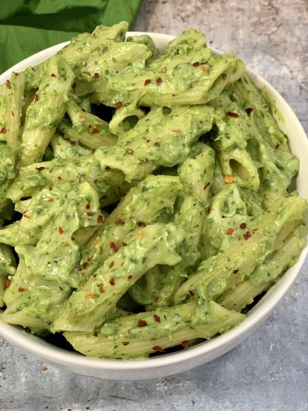 A beautiful bowl of creamy green avocado pasta, garnished with cherry tomatoes, pine nuts, and microgreens.